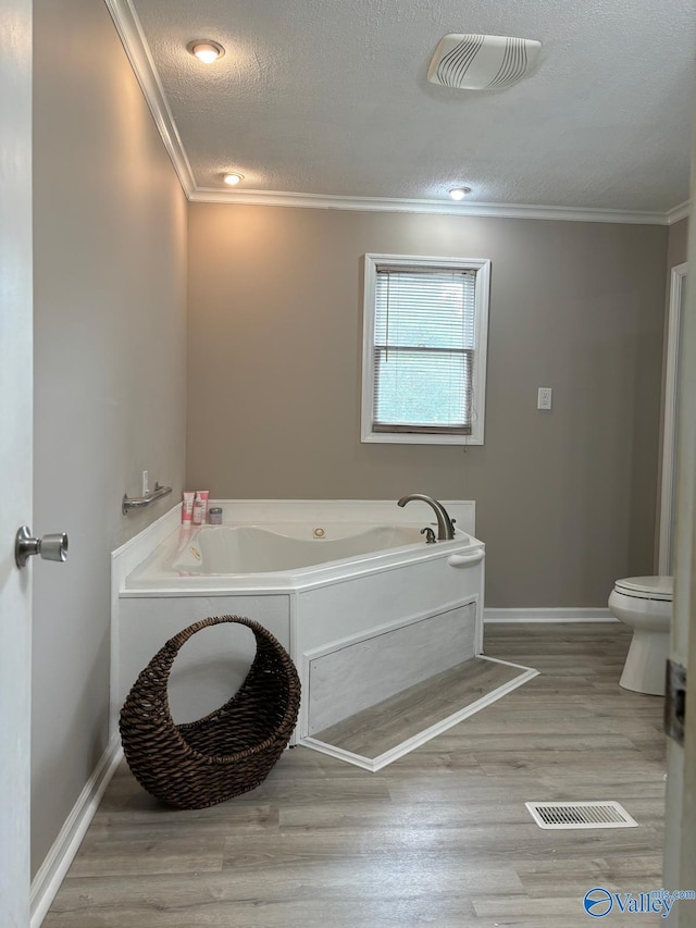 bathroom with toilet, crown molding, a textured ceiling, hardwood / wood-style flooring, and a washtub