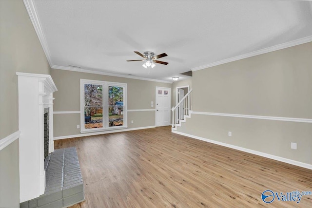 unfurnished living room featuring crown molding, baseboards, ceiling fan, a brick fireplace, and wood finished floors
