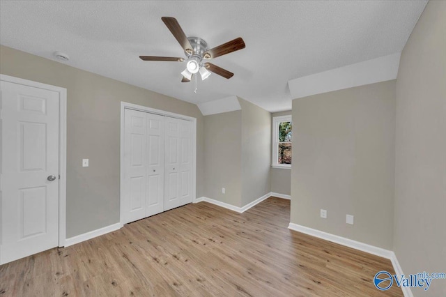 unfurnished bedroom featuring a closet, a ceiling fan, a textured ceiling, baseboards, and light wood-style floors