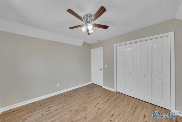 unfurnished bedroom with vaulted ceiling, a closet, wood finished floors, baseboards, and ceiling fan
