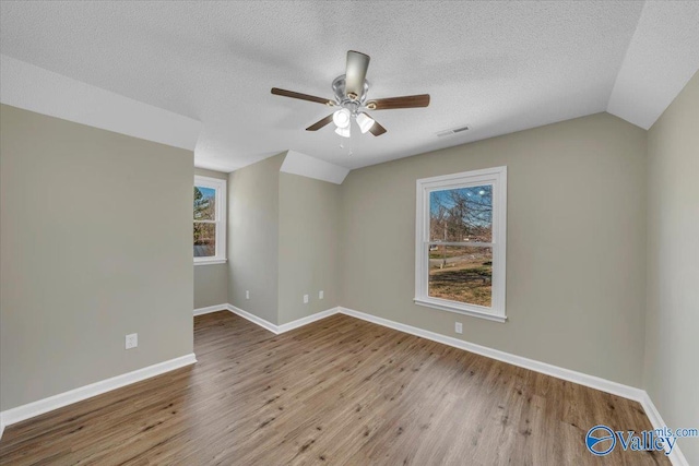 empty room with visible vents, baseboards, wood finished floors, a ceiling fan, and vaulted ceiling