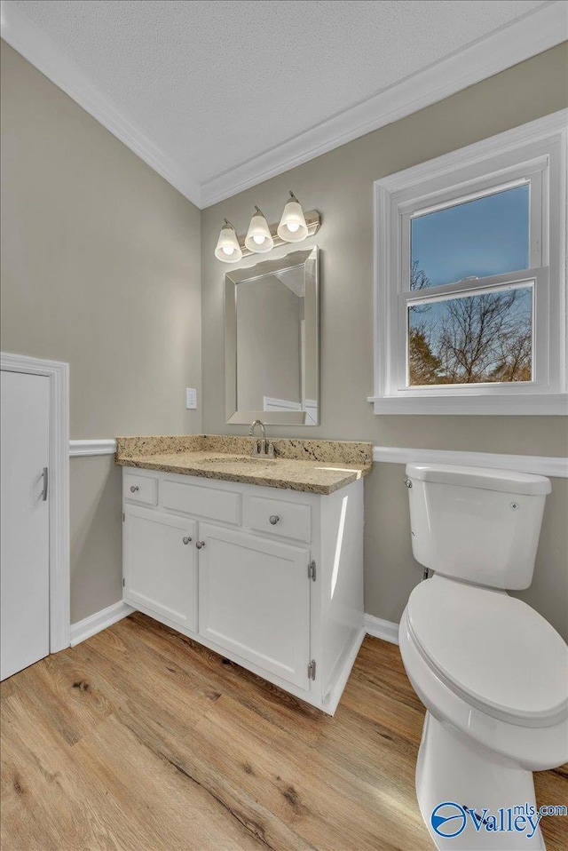 half bath with crown molding, toilet, vanity, wood finished floors, and a textured ceiling