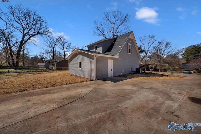 view of side of property with central air condition unit, a shingled roof, fence, and concrete driveway