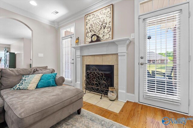 living area with visible vents, a tiled fireplace, arched walkways, wood finished floors, and ornamental molding