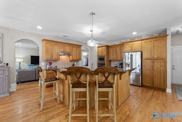 kitchen featuring appliances with stainless steel finishes, arched walkways, tasteful backsplash, under cabinet range hood, and a kitchen bar