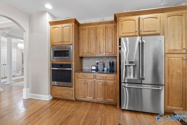 kitchen featuring baseboards, light wood-type flooring, tasteful backsplash, arched walkways, and stainless steel appliances