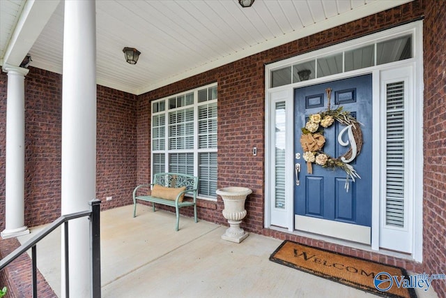 view of exterior entry featuring covered porch and brick siding