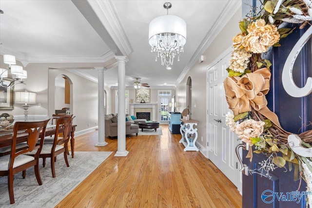 foyer with ornamental molding, a fireplace, baseboards, ornate columns, and light wood finished floors