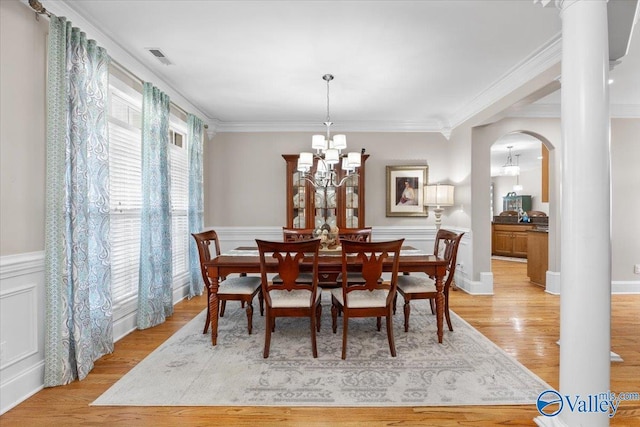 dining area with crown molding, an inviting chandelier, wainscoting, light wood finished floors, and arched walkways