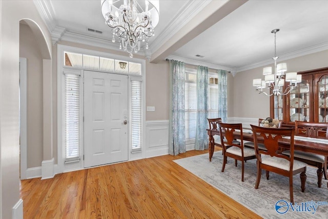 dining space featuring an inviting chandelier, arched walkways, ornamental molding, and light wood-style flooring