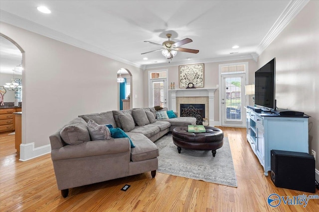 living room featuring arched walkways, ornamental molding, ceiling fan with notable chandelier, and light wood finished floors