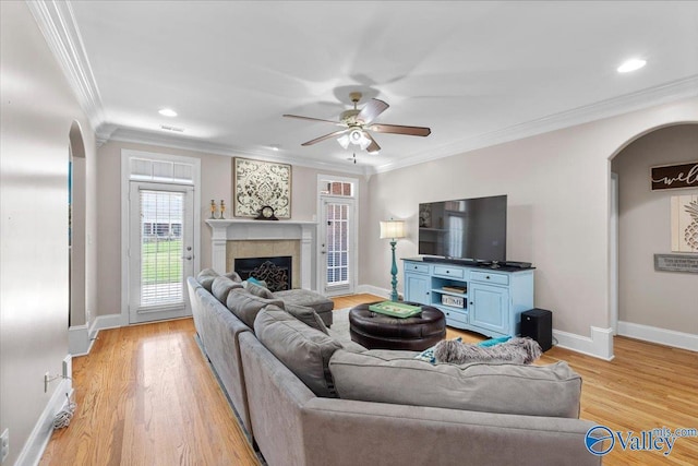 living room with crown molding, arched walkways, ceiling fan, and baseboards