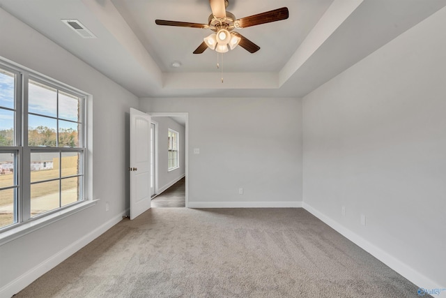 carpeted spare room featuring a ceiling fan, a raised ceiling, baseboards, and visible vents