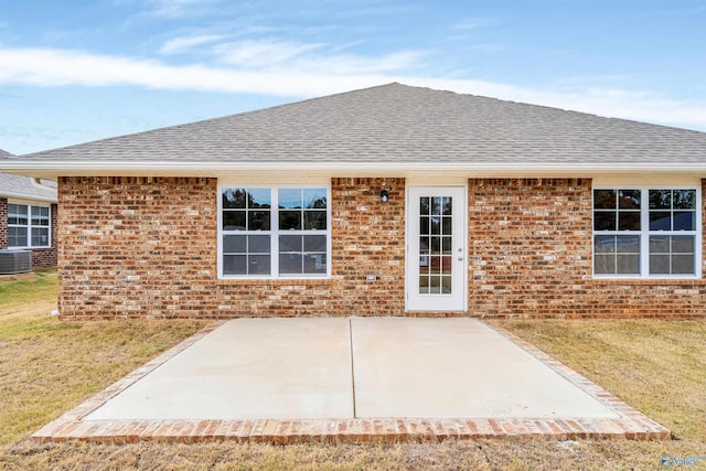 rear view of property featuring brick siding, a yard, a shingled roof, and a patio