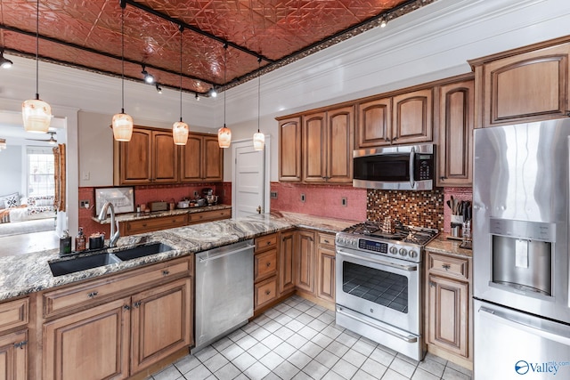 kitchen with tasteful backsplash, hanging light fixtures, appliances with stainless steel finishes, light stone countertops, and sink