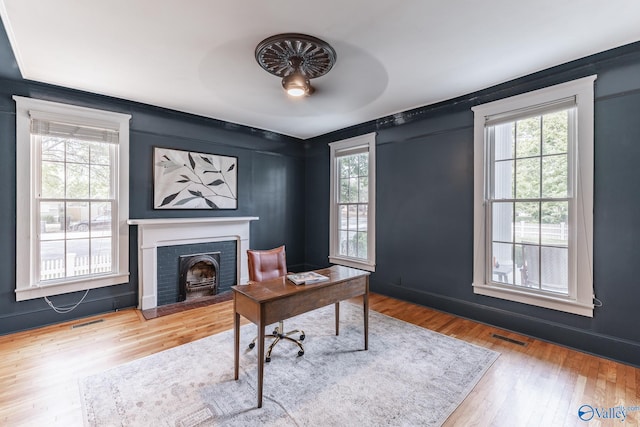 office with hardwood / wood-style floors, a healthy amount of sunlight, ceiling fan, and a brick fireplace