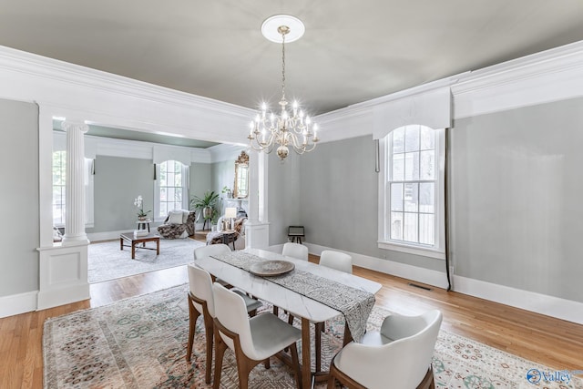 dining space featuring ornamental molding, a chandelier, light hardwood / wood-style flooring, and ornate columns