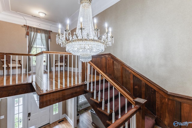 stairway with a wealth of natural light, ornamental molding, hardwood / wood-style floors, and an inviting chandelier