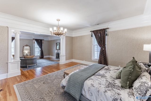 bedroom featuring multiple windows, ornamental molding, wood-type flooring, and decorative columns