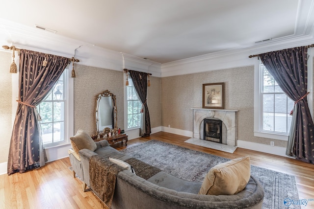 living room with a wealth of natural light, ornamental molding, a fireplace, and light hardwood / wood-style floors