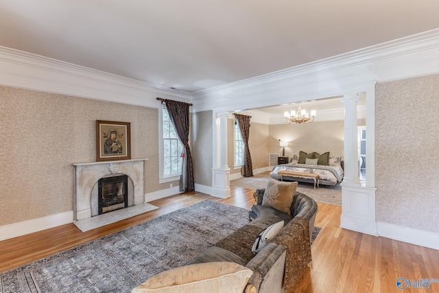 living room with a premium fireplace, decorative columns, crown molding, an inviting chandelier, and light hardwood / wood-style floors