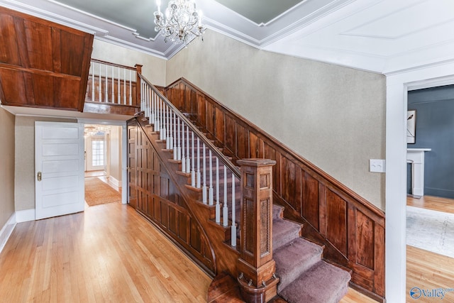 staircase with hardwood / wood-style floors, crown molding, a chandelier, and wood walls