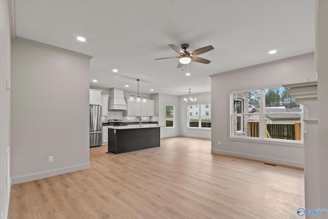 kitchen with appliances with stainless steel finishes, white cabinetry, premium range hood, an island with sink, and decorative light fixtures