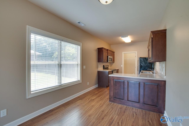 kitchen featuring light hardwood / wood-style flooring, tasteful backsplash, appliances with stainless steel finishes, sink, and kitchen peninsula