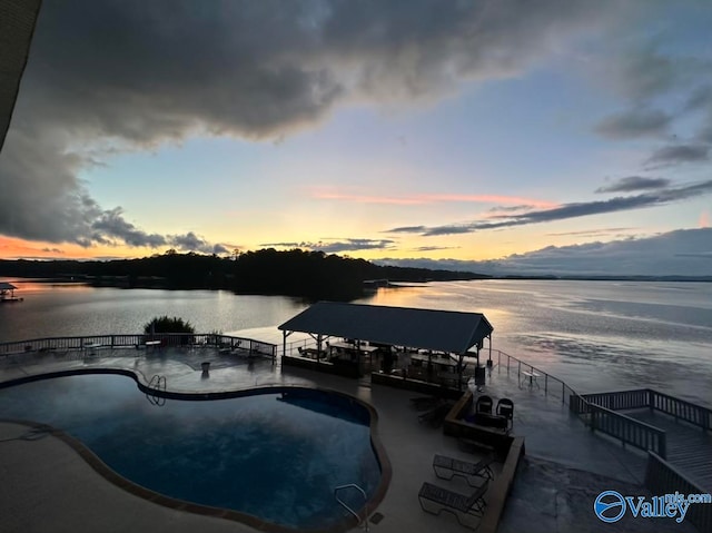 pool at dusk featuring a patio area and a water view