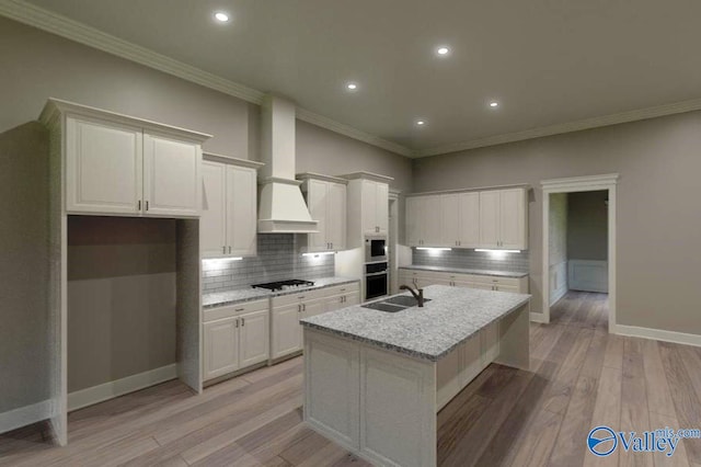 kitchen featuring light wood-style floors, custom exhaust hood, backsplash, and a sink