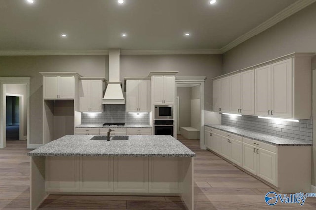 kitchen featuring wall oven, a kitchen island with sink, a sink, built in microwave, and stovetop