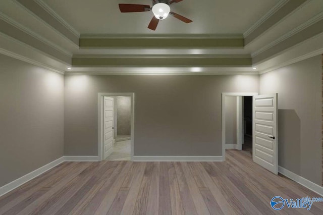 unfurnished room with ornamental molding, a tray ceiling, wood finished floors, and baseboards