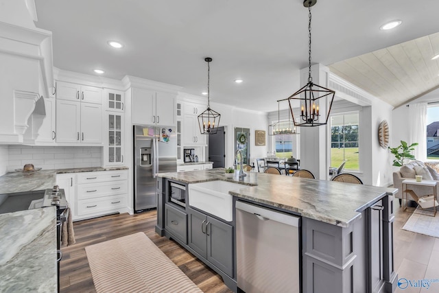 kitchen with an island with sink, stainless steel appliances, white cabinets, dark wood-type flooring, and decorative light fixtures