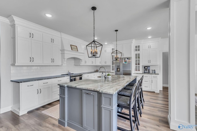 kitchen featuring white cabinets, an island with sink, pendant lighting, stainless steel appliances, and dark hardwood / wood-style flooring