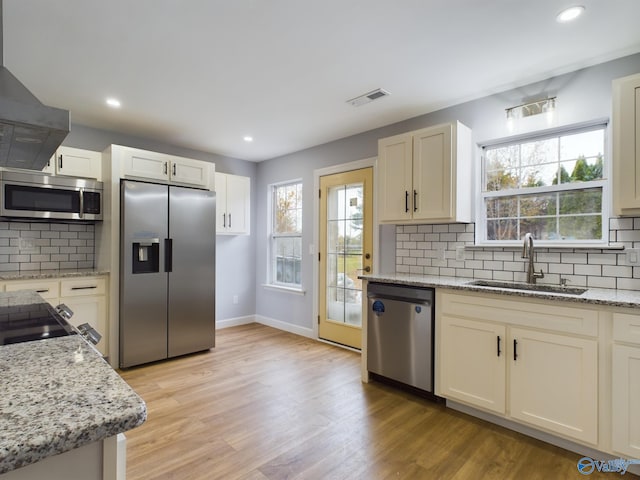 kitchen with stainless steel appliances, sink, backsplash, range hood, and light hardwood / wood-style flooring