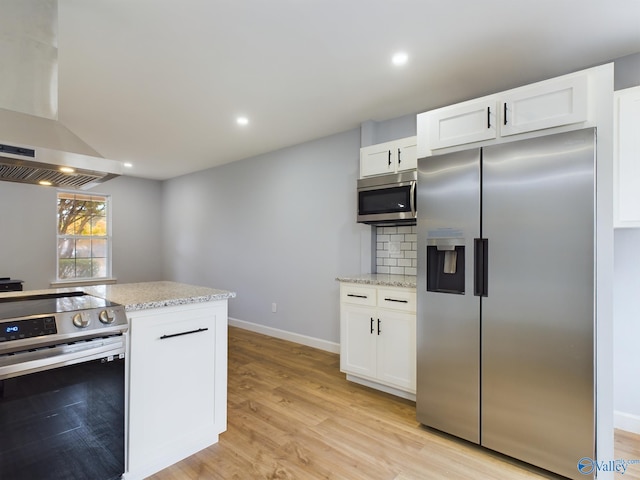 kitchen with light hardwood / wood-style floors, appliances with stainless steel finishes, light stone countertops, wall chimney exhaust hood, and white cabinets