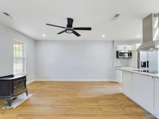 living room with ceiling fan, a wood stove, and light hardwood / wood-style flooring