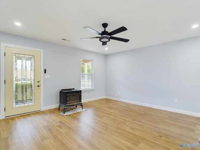 unfurnished living room with ceiling fan, a wood stove, and light hardwood / wood-style floors