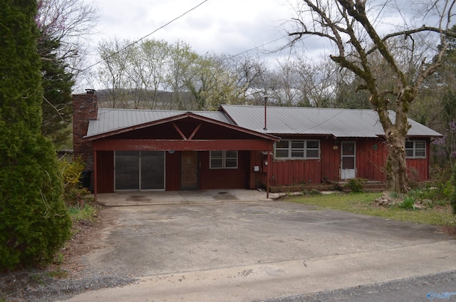 single story home with metal roof, board and batten siding, driveway, an attached carport, and a chimney