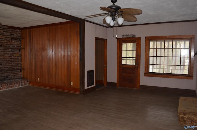 unfurnished living room featuring wooden walls, crown molding, wood finished floors, and a ceiling fan