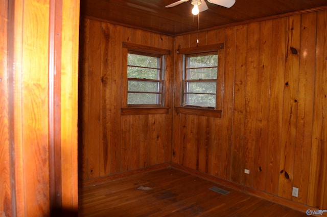 empty room featuring wood-type flooring, ceiling fan, visible vents, and wood walls