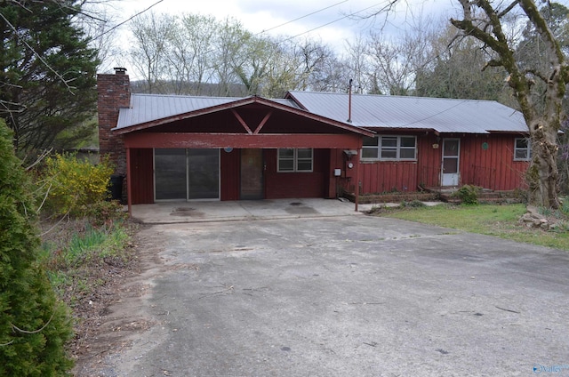 single story home featuring a chimney, driveway, a carport, and metal roof