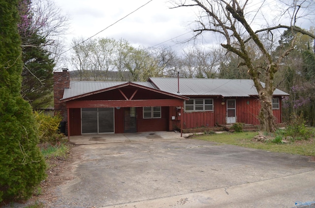 ranch-style house with a chimney, an attached carport, concrete driveway, and metal roof