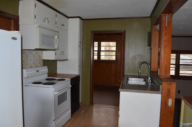 kitchen featuring wood walls, white cabinets, a sink, and white appliances