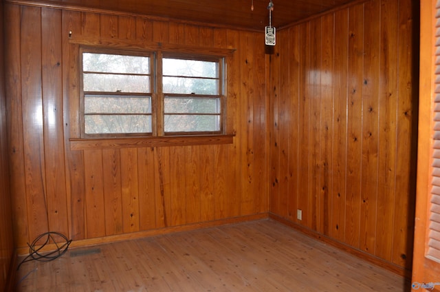 spare room with wood-type flooring, baseboards, wooden walls, and visible vents