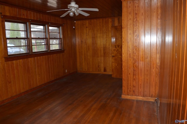 empty room featuring wood finished floors, baseboards, wooden walls, and ceiling fan
