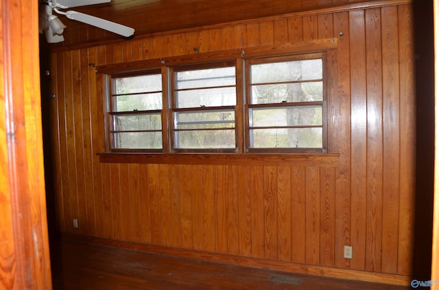unfurnished room with visible vents, wooden walls, wood finished floors, and a ceiling fan
