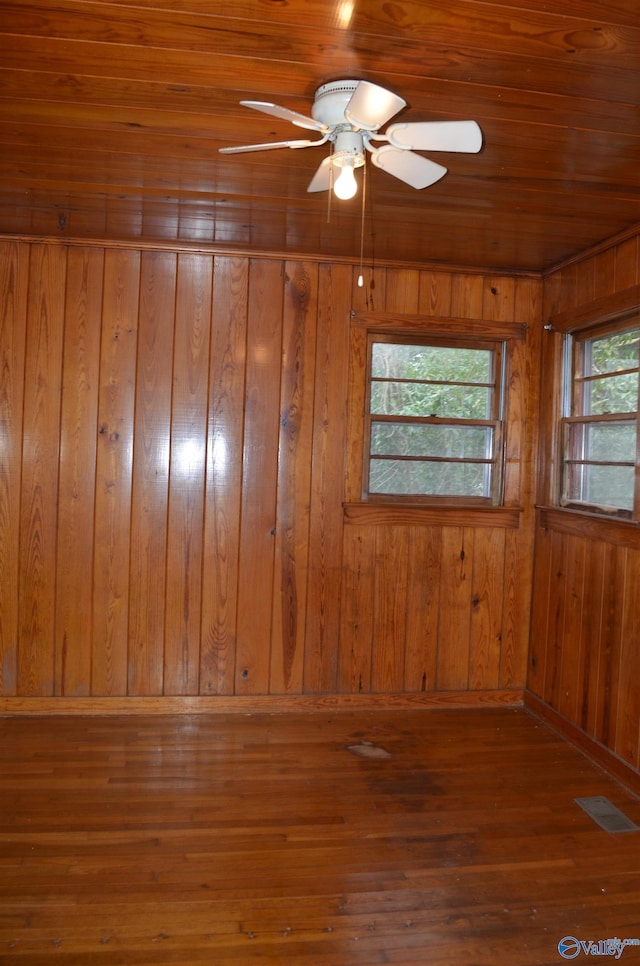 spare room featuring hardwood / wood-style floors, visible vents, wood walls, and ceiling fan