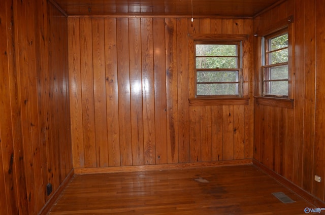 spare room featuring wood-type flooring, wooden walls, and visible vents