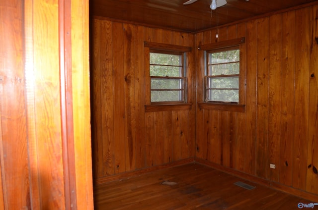 spare room with visible vents, a ceiling fan, wood walls, and hardwood / wood-style floors